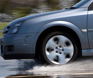 Blue car tire splashes through wet pavement, suggesting traction and handling in rainy conditions.