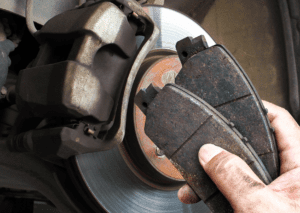 Mechanic holding worn brake pads near a car's brake disc, showing clear signs to replace brake pads for safety.