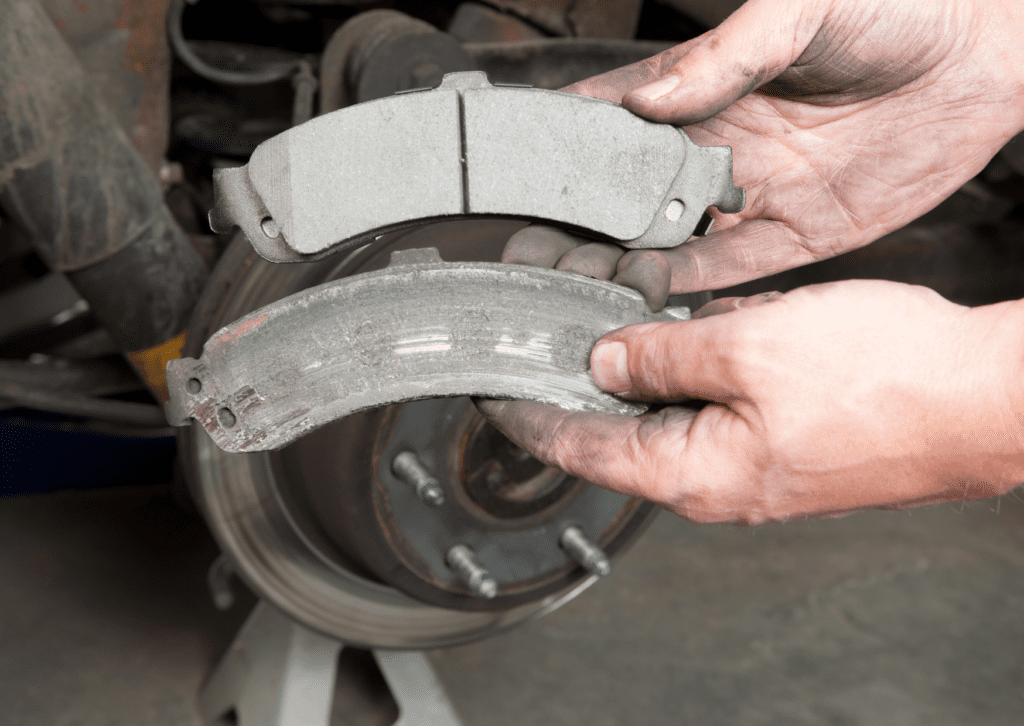 Mechanic holding a worn brake pad next to a new one, highlighting the need for brake pad replacement.