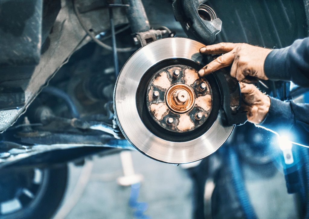 Mechanic inspecting a car’s brake disc and caliper, ensuring proper brake function and safety in a repair shop.