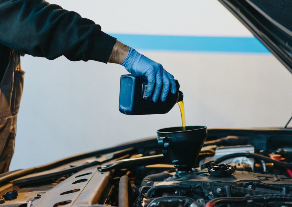 Mechanic wearing blue gloves pouring fresh engine oil into a car using a funnel during routine maintenance.