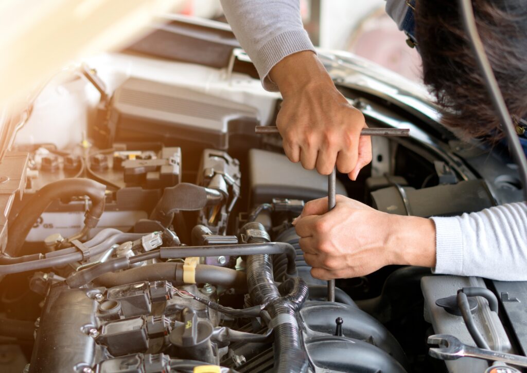 Mechanic using a wrench to repair a car engine, performing maintenance and adjustments under the hood.