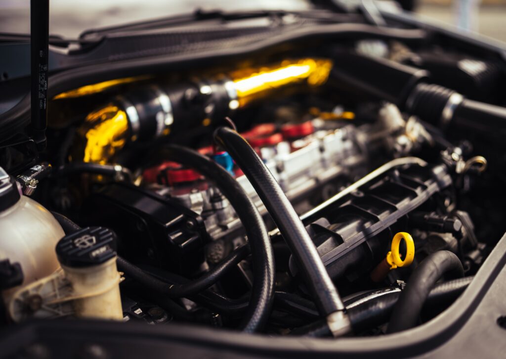Close-up view of a high-performance car engine with hoses, wires, and a reflective heat-wrapped intake pipe.