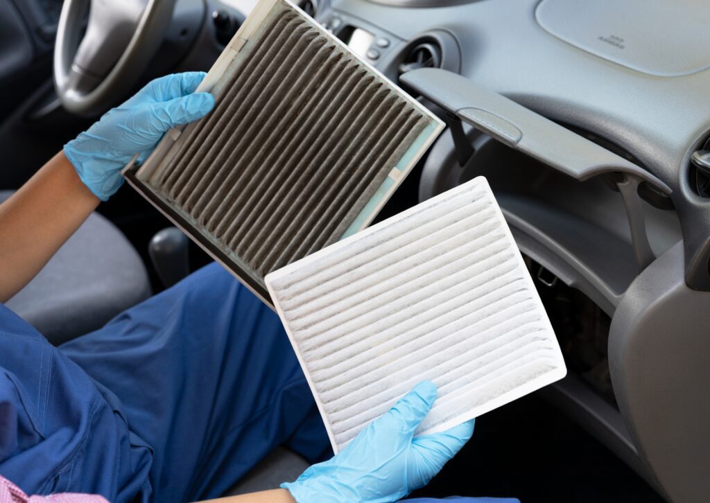 Mechanic in blue gloves holding a dirty and clean cabin air filter inside a car, showing the importance of replacement