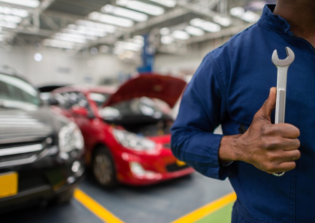 Mechanic in blue uniform holding a wrench in a busy auto repair shop with cars being serviced in the background