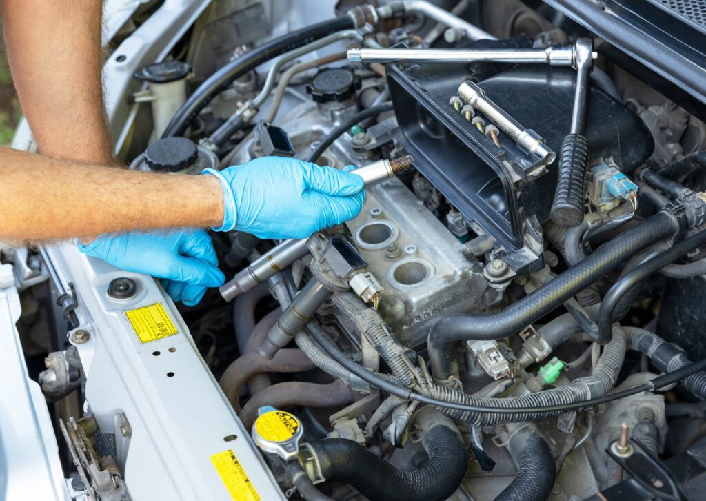 Mechanic wearing blue gloves replacing a spark plug in a car engine during maintenance with tools on the side