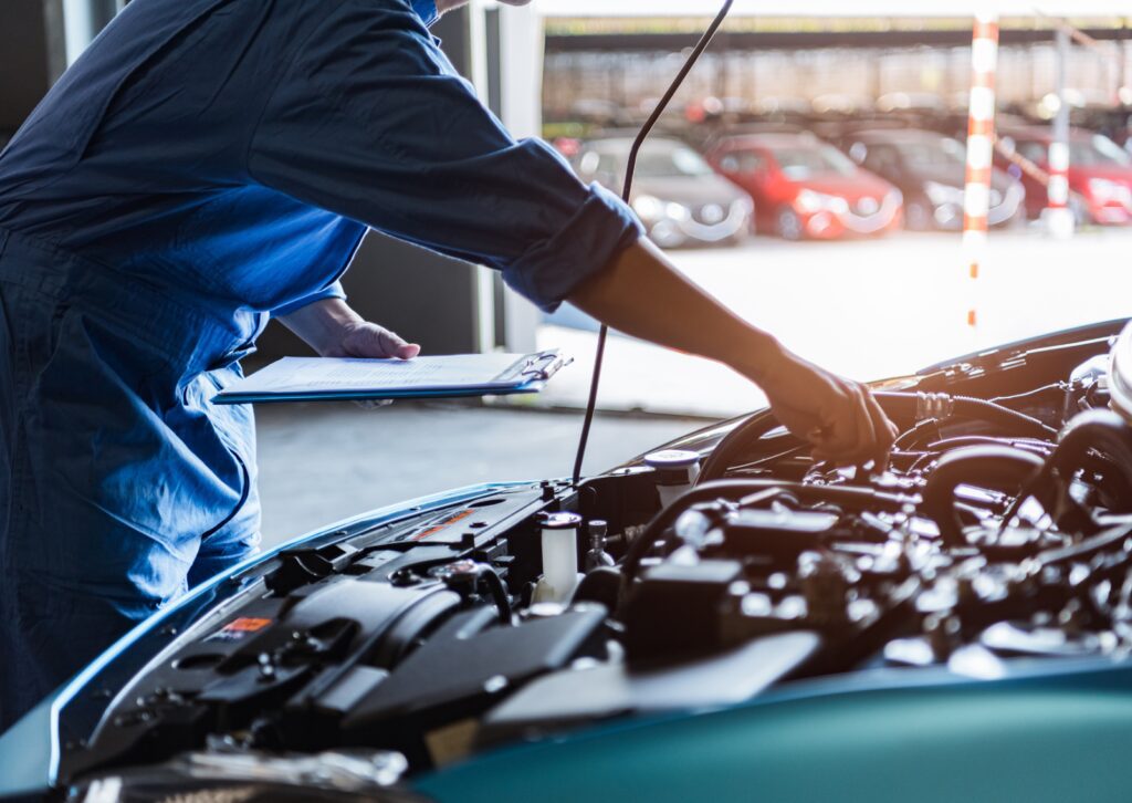 Mechanic inspecting a car engine with a clipboard, demonstrating what is a tune-up for vehicle maintenance.