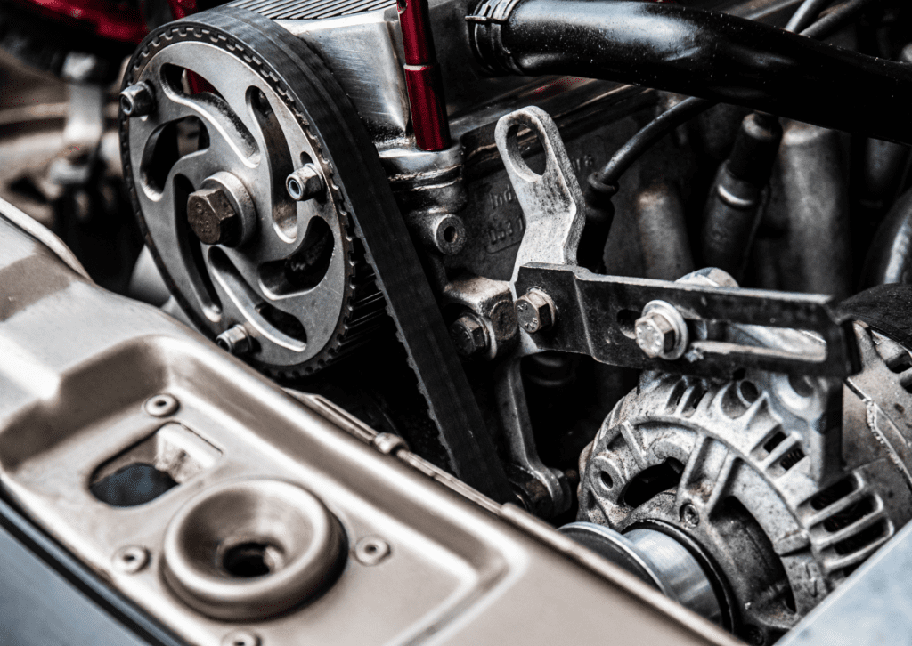 Close-up of a car engine showing the timing belt, pulleys, and alternator with detailed mechanical components.