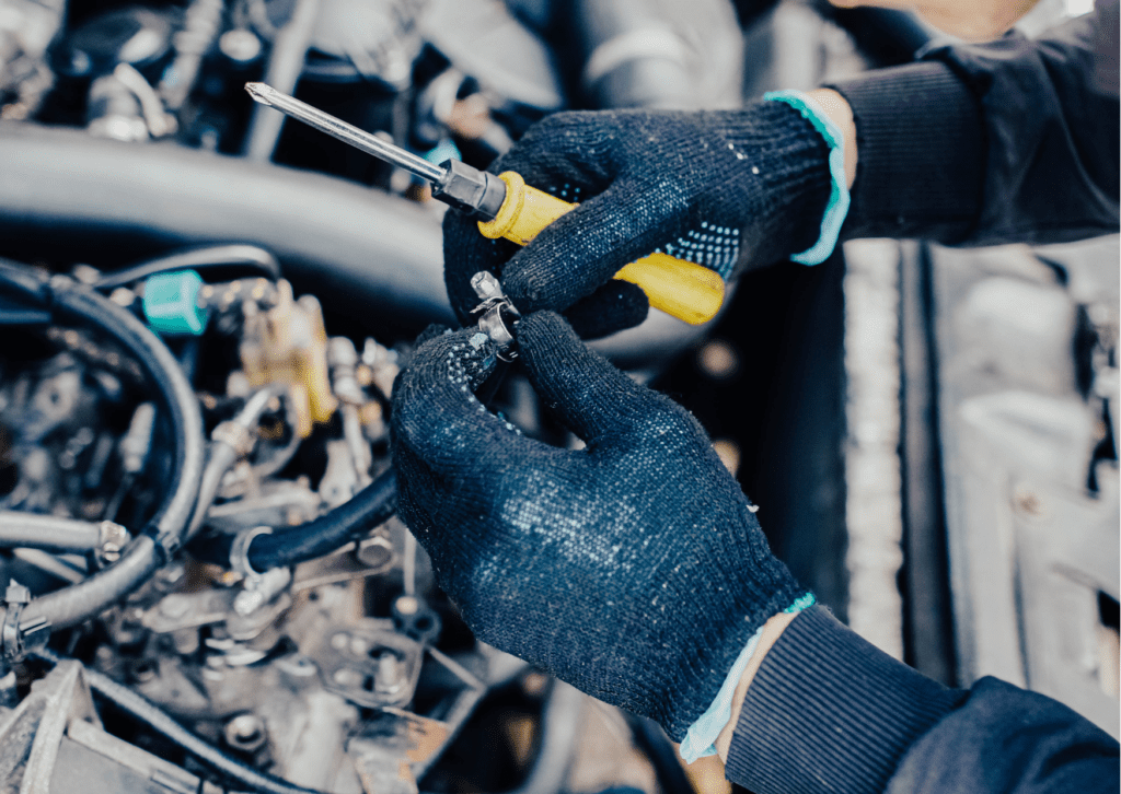 Mechanic wearing gloves uses a screwdriver to fix a fuel hose clamp. Fuel system problems impact performance.