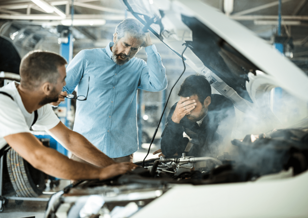 Three worried men inspecting a smoking car engine in a garage, signaling a serious mechanical issue.