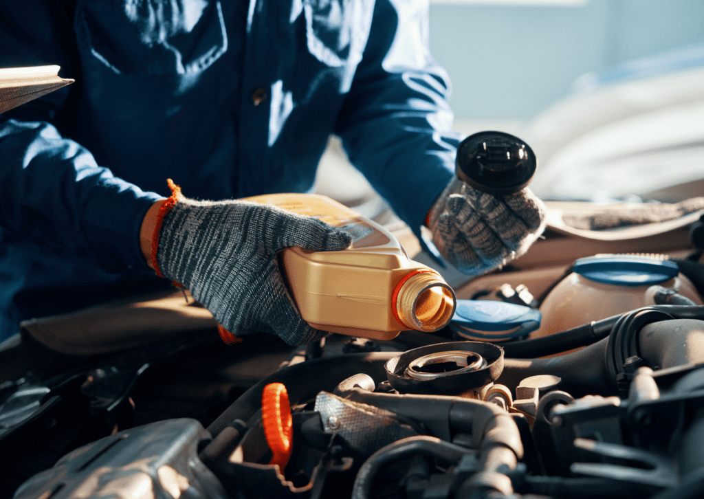 Mechanic in gloves and blue uniform preparing to pour engine oil into a car during maintenance.