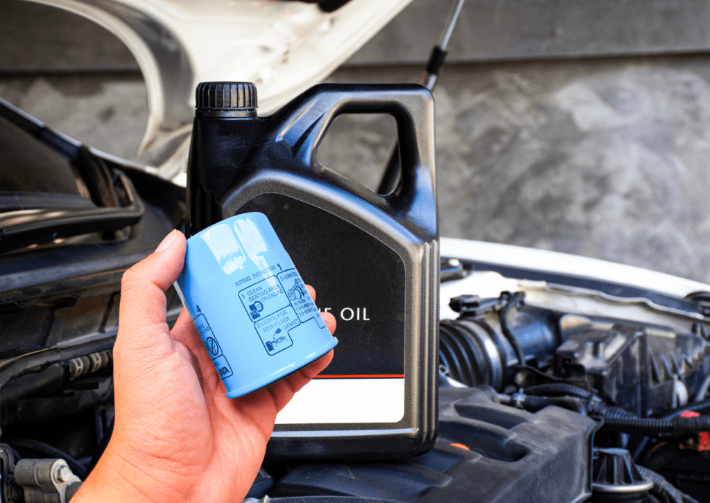 Hand holding a blue oil filter with a black engine oil container in the background during car maintenance.