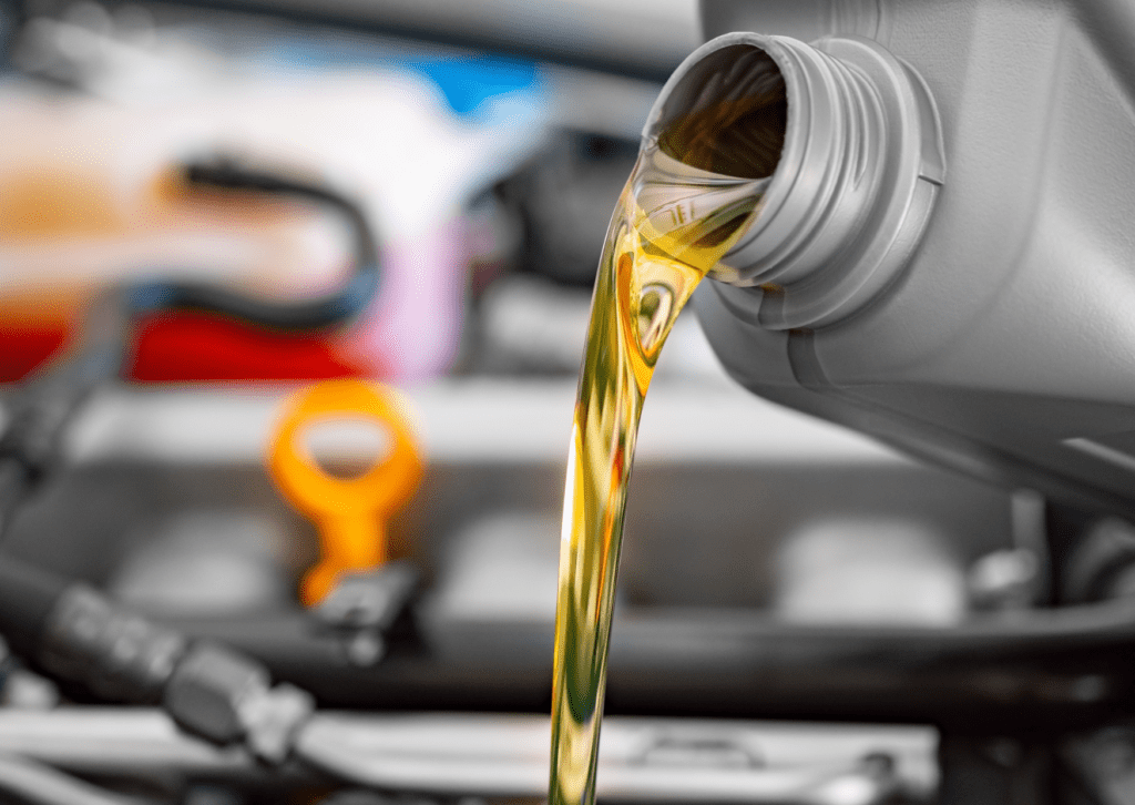 Golden engine oil being poured from a gray container into a car engine during an oil change maintenance.
