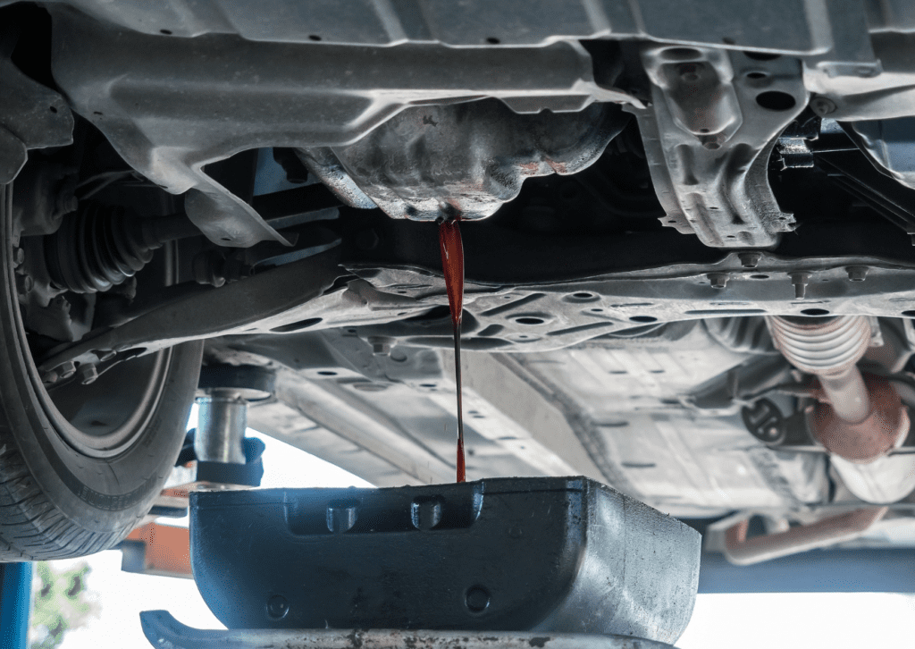 Car oil draining from the engine into a container during an oil change in an automotive repair shop.
