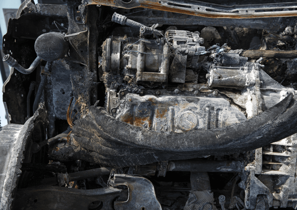 Burned and damaged car engine with melted components and charred wires after a severe fire accident.