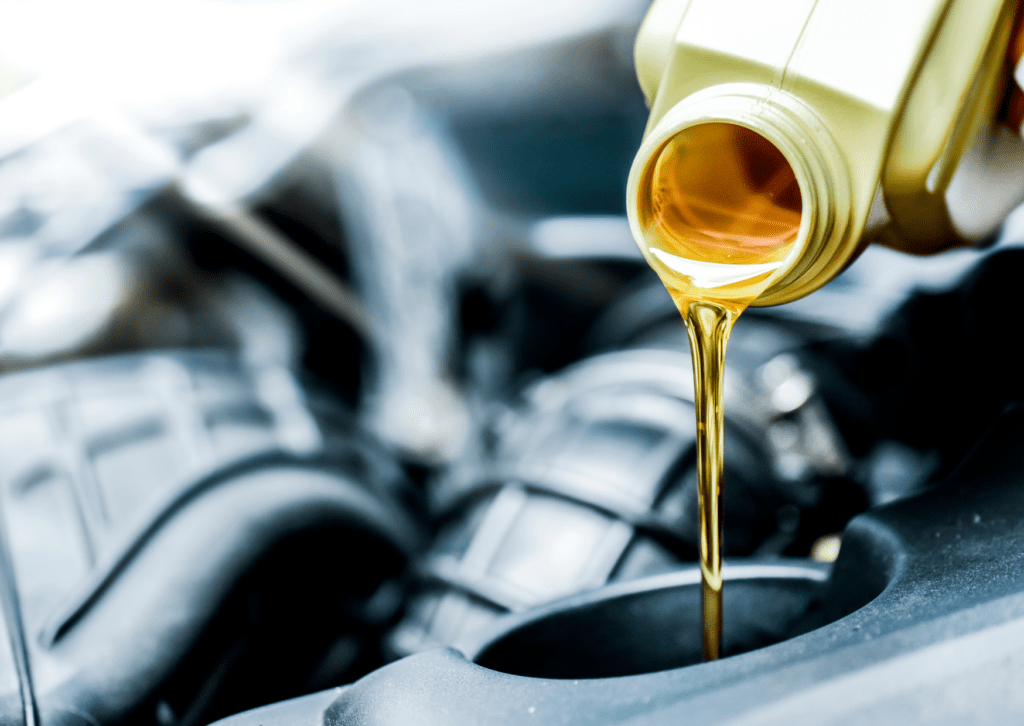 Golden engine oil being poured from a bottle into a car engine for maintenance and lubrication.