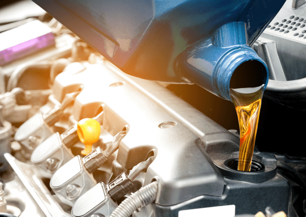 Golden engine oil being poured from a blue container into a car engine during an oil change maintenance.