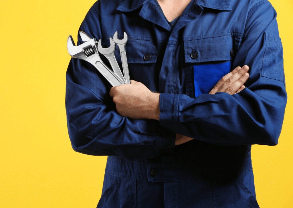 Mechanic in blue uniform holding metal wrenches across chest against bright yellow background