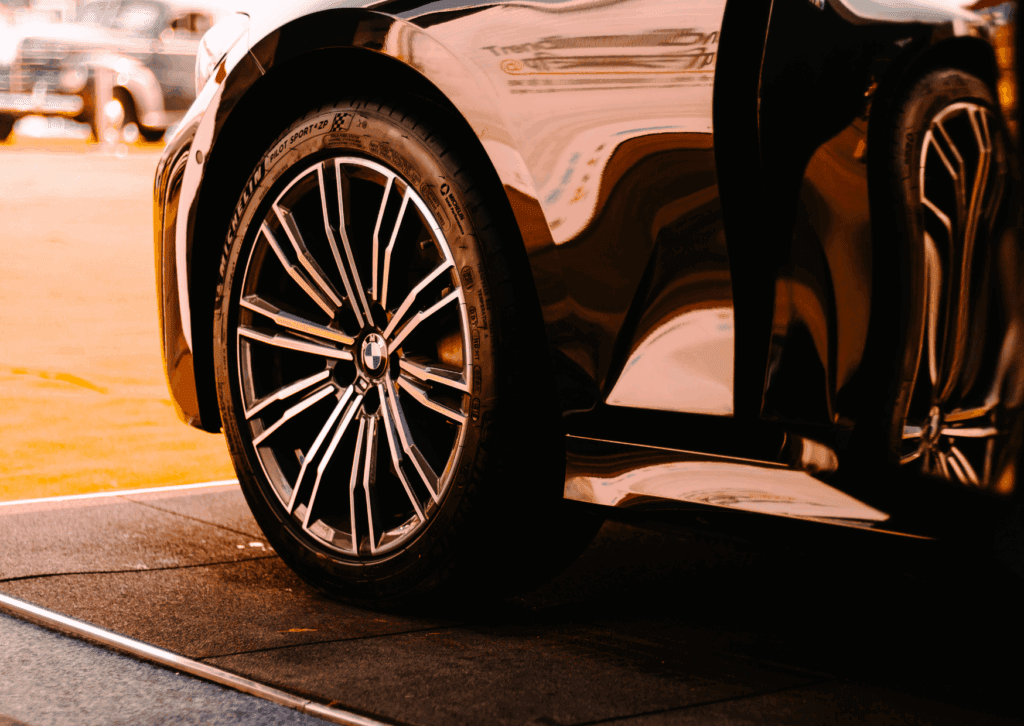 Close-up of BMW wheel and tire on a shiny black car parked on pavement in warm sunlight.