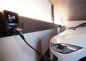 Home garage wall EV charger powers a white electric car, screen shows 3.49 kW; battery health diagnostics for EV.