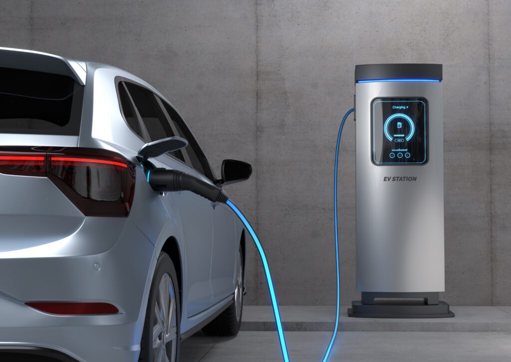 Silver EV plugged into charging station with blue cable by concrete wall; battery health diagnostics for EV services.