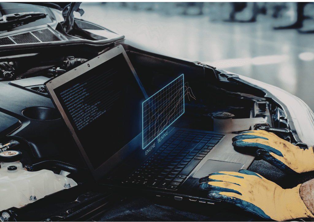 Technician uses laptop for car diagnostics on open engine bay in workshop, with engine tuning graph overlay.
