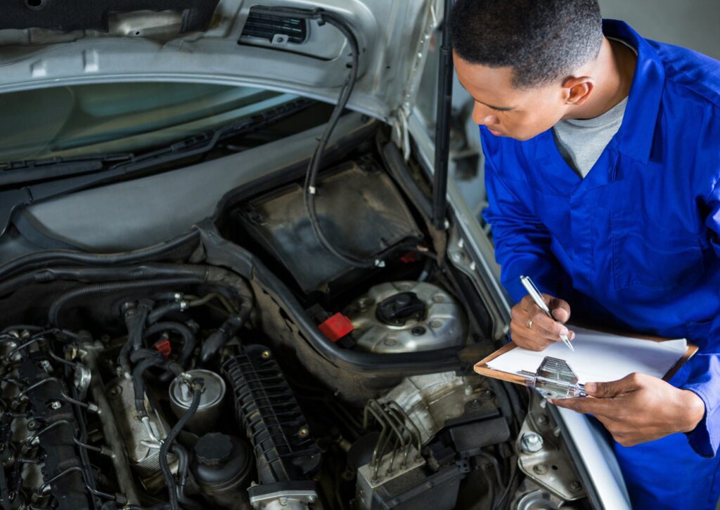 Technician inspects engine bay and writes checklist during Toyota car maintenance service with hood open in shop.