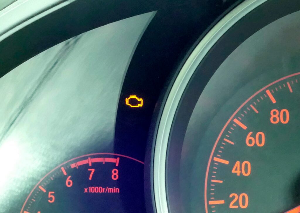 Dashboard cluster showing check engine light flashing beside tachometer and speedometer at idle.