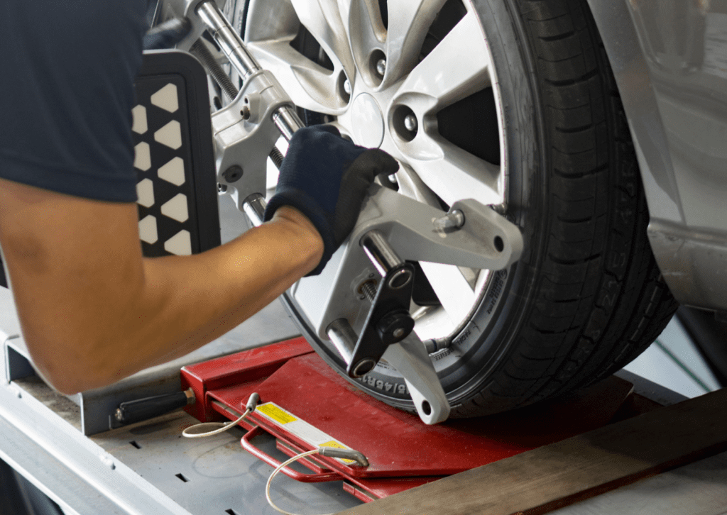 Technician performs wheel alignment on car tire using precision equipment in auto service bay.