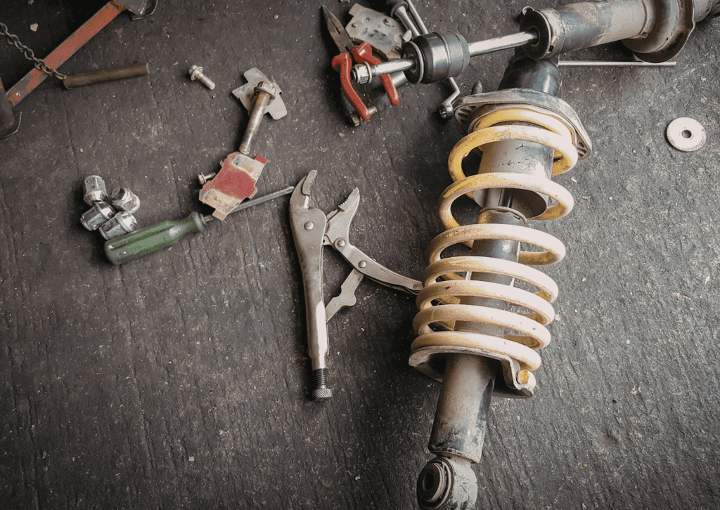 Shock absorber and coil spring removed with tools laid out for vehicle suspension repair work.

