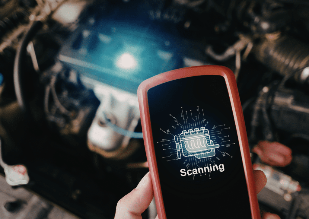 Hand holds diagnostic scanner in front of open engine bay during electronic vehicle system check.