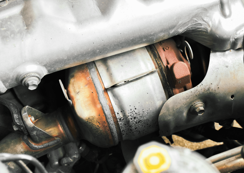 Close-up of catalytic converter and exhaust component inside engine bay during vehicle inspection.