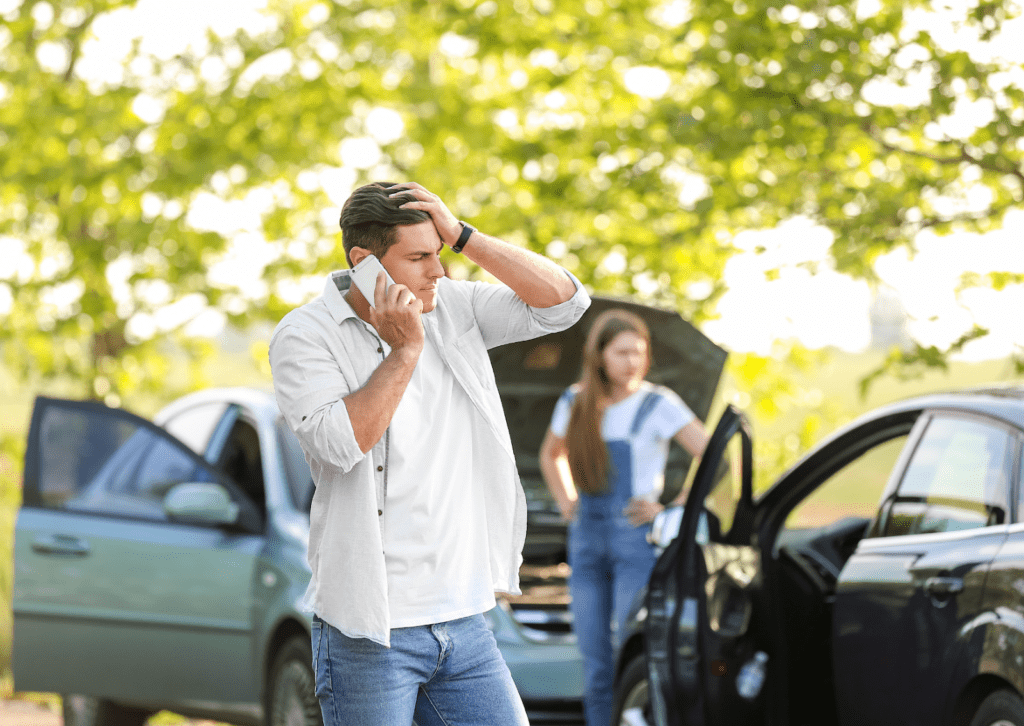Driver calls for help beside broken-down cars while passenger waits by open hood at roadside.