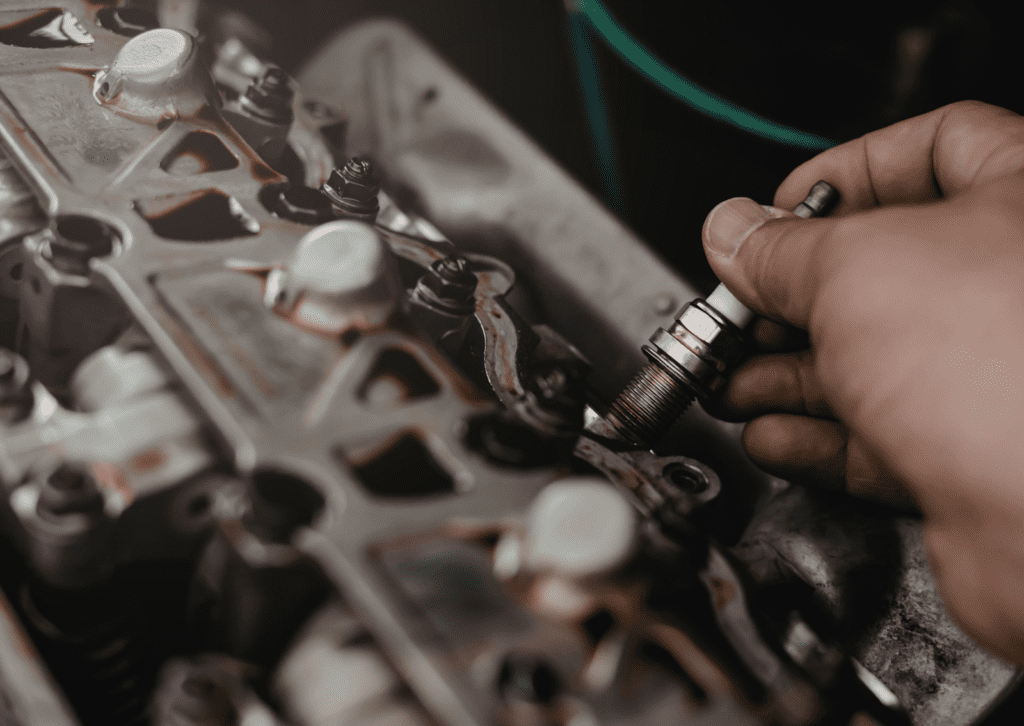 Hand installing spark plug into engine head during vehicle tune-up and repair service work.