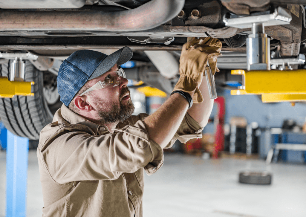 Mechanic inspects undercarriage of lifted vehicle while performing maintenance in auto repair shop.