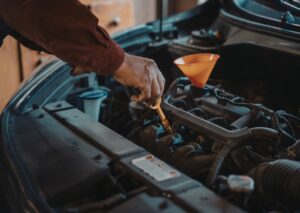 Hand checking engine oil dipstick with funnel in open engine bay for types-of-car-leaks inspection.
