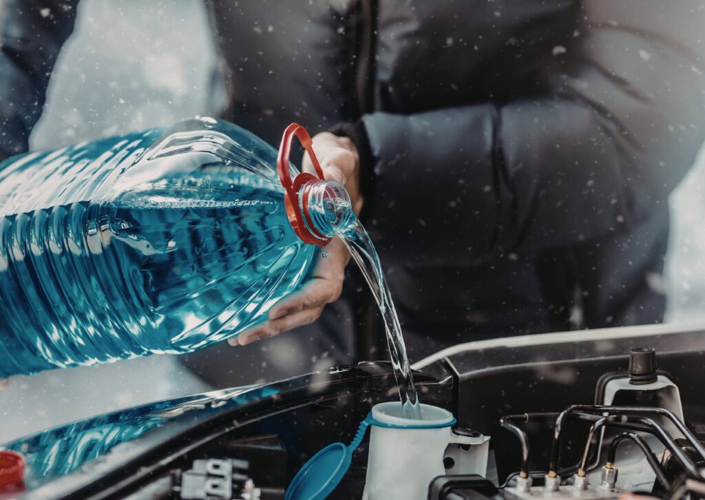 Person pouring blue fluid into engine reservoir in winter, illustrating types-of-car-leaks checks.