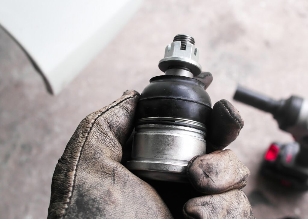 Gloved hand holding ball joint part during repair, showing what are the 3 common suspension noises