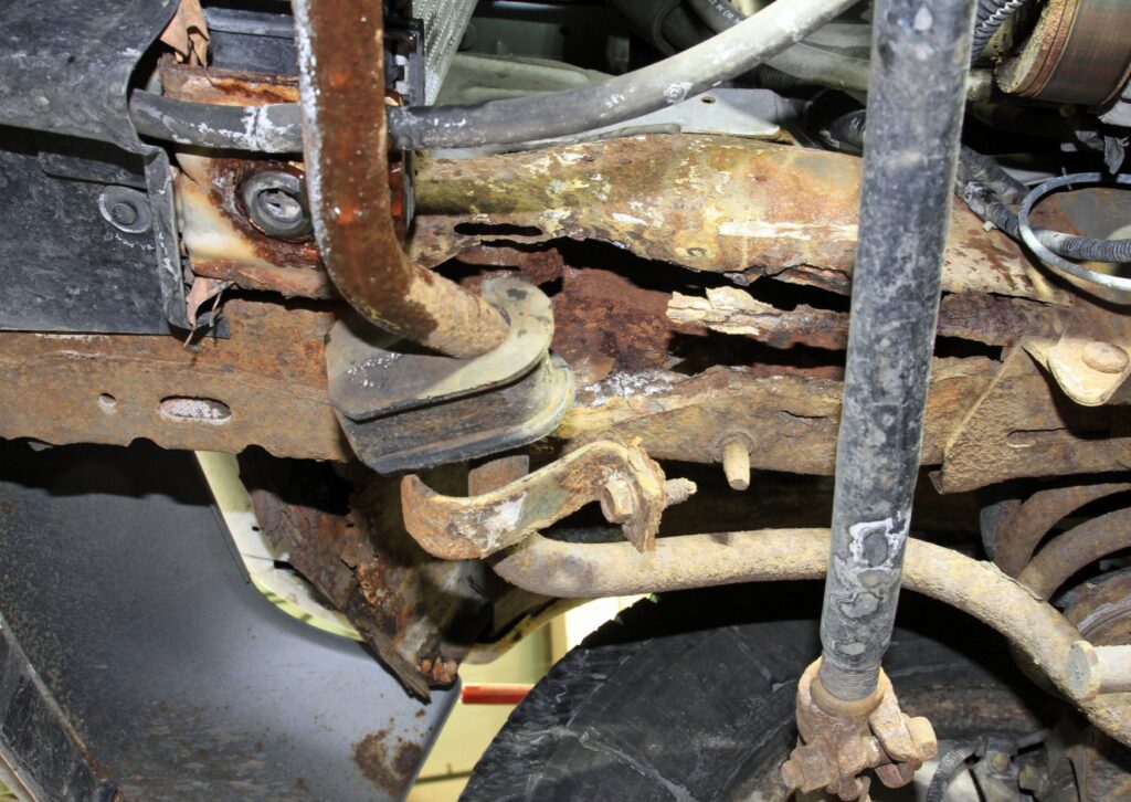 Close-up of rusted vehicle undercarriage showing corroded frame, suspension and severe metal damage.