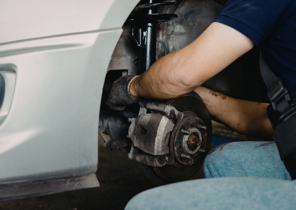 Mechanic repairing brake and suspension assembly inside wheel well during vehicle service work.
