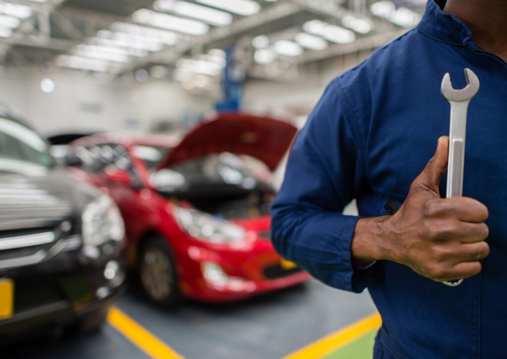 Mechanic holding wrench in auto shop with cars in service bays, ready for professional repairs.