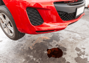 Red car leaking fluid when parked with dark puddle beneath front bumper in repair garage bay 