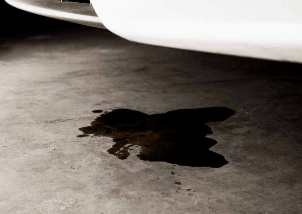 Dark fluid puddle on garage floor beneath a white car, showing possible vehicle leak repairs 
