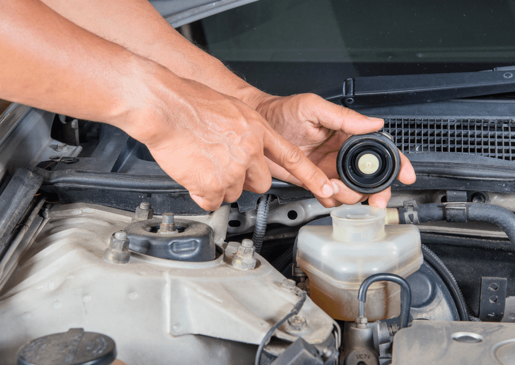Hands removing brake fluid reservoir cap in engine bay during vehicle maintenance inspection 