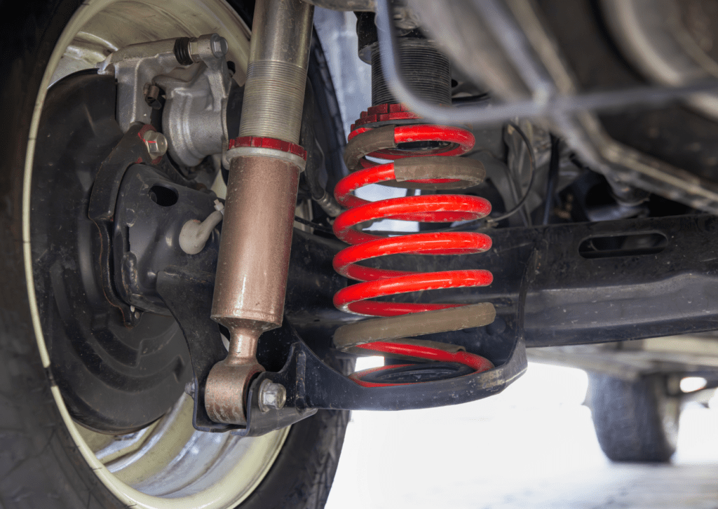 Close-up of red coil spring and shock absorber under a vehicle during suspension inspection 