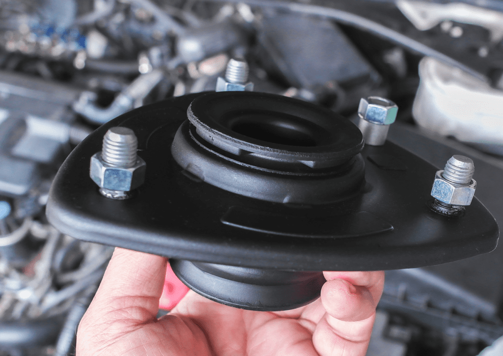 Hand holding a new strut mount above an engine bay during suspension repair and inspection 