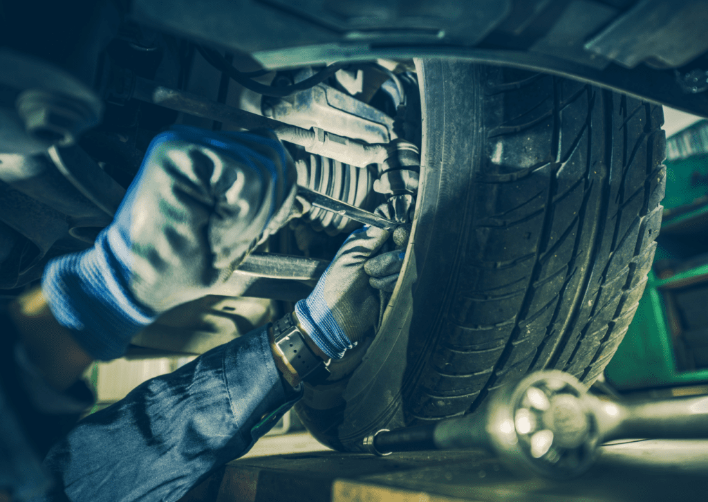 Mechanic inspecting steering and suspension parts behind a car tire during underbody repair service 