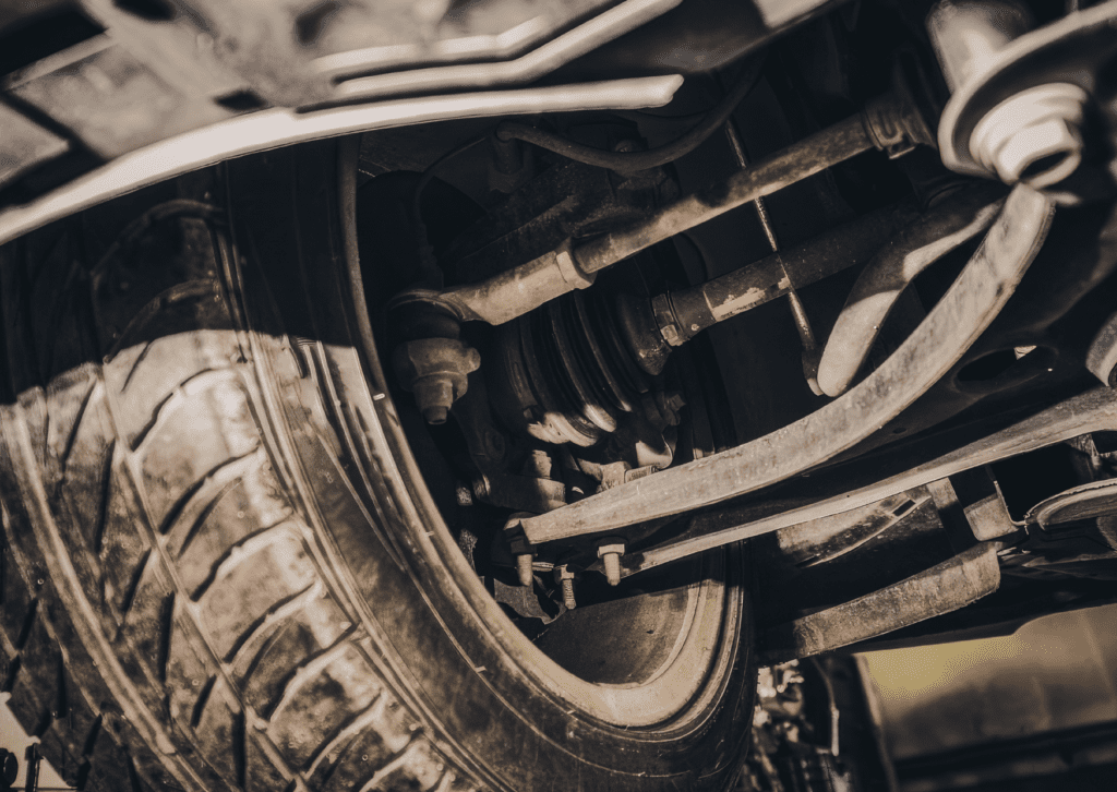Close-up view of vehicle suspension, tire, and steering parts underneath a raised car for repair 