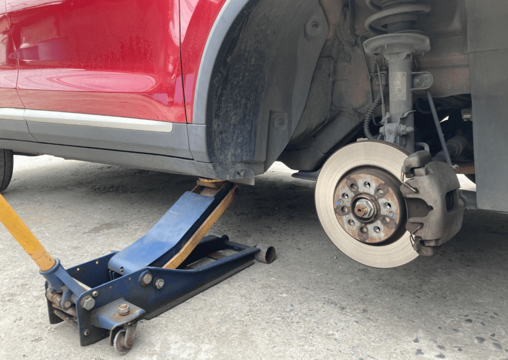 Red car raised on a floor jack with wheel removed for inspection of car clunking noise issue 