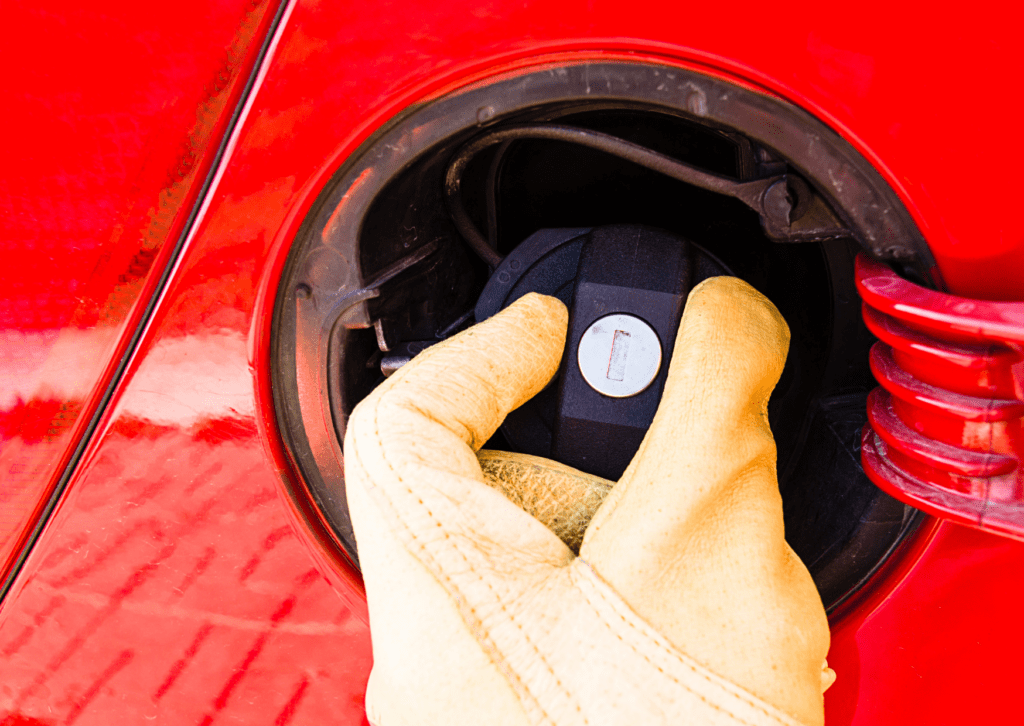 Gloved hand tightening the fuel cap on a red car during maintenance near the gas door opening 